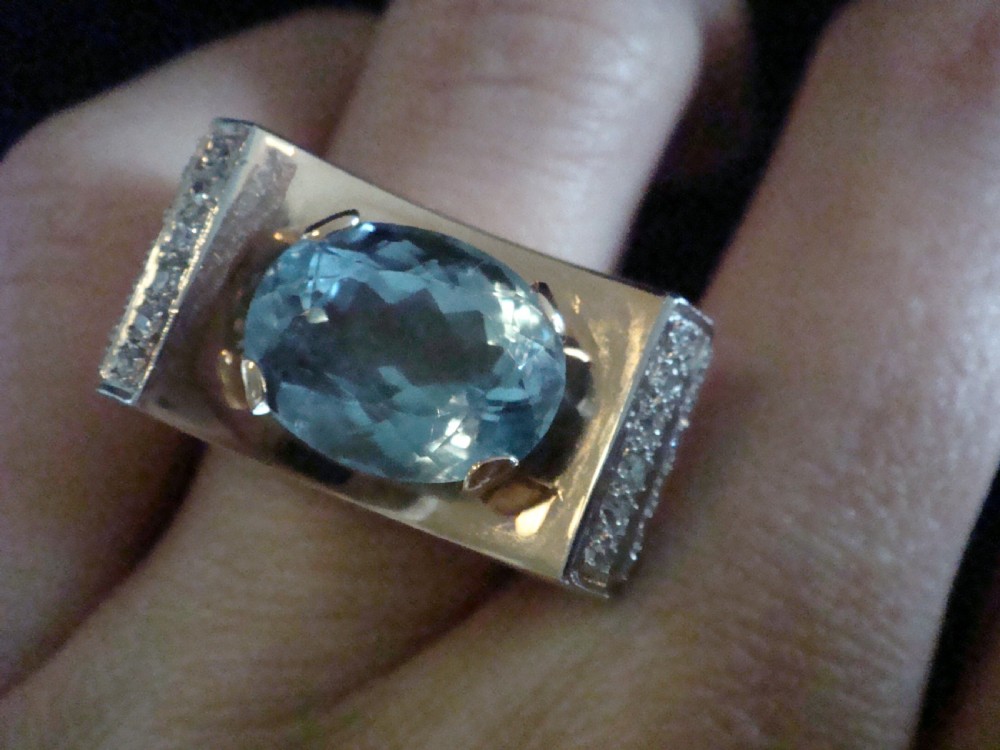 An antique French Tank ring featuring an oval faceted light blue topaz set in gold, framed by broad platinum shoulders set with small accent diamonds. View VI