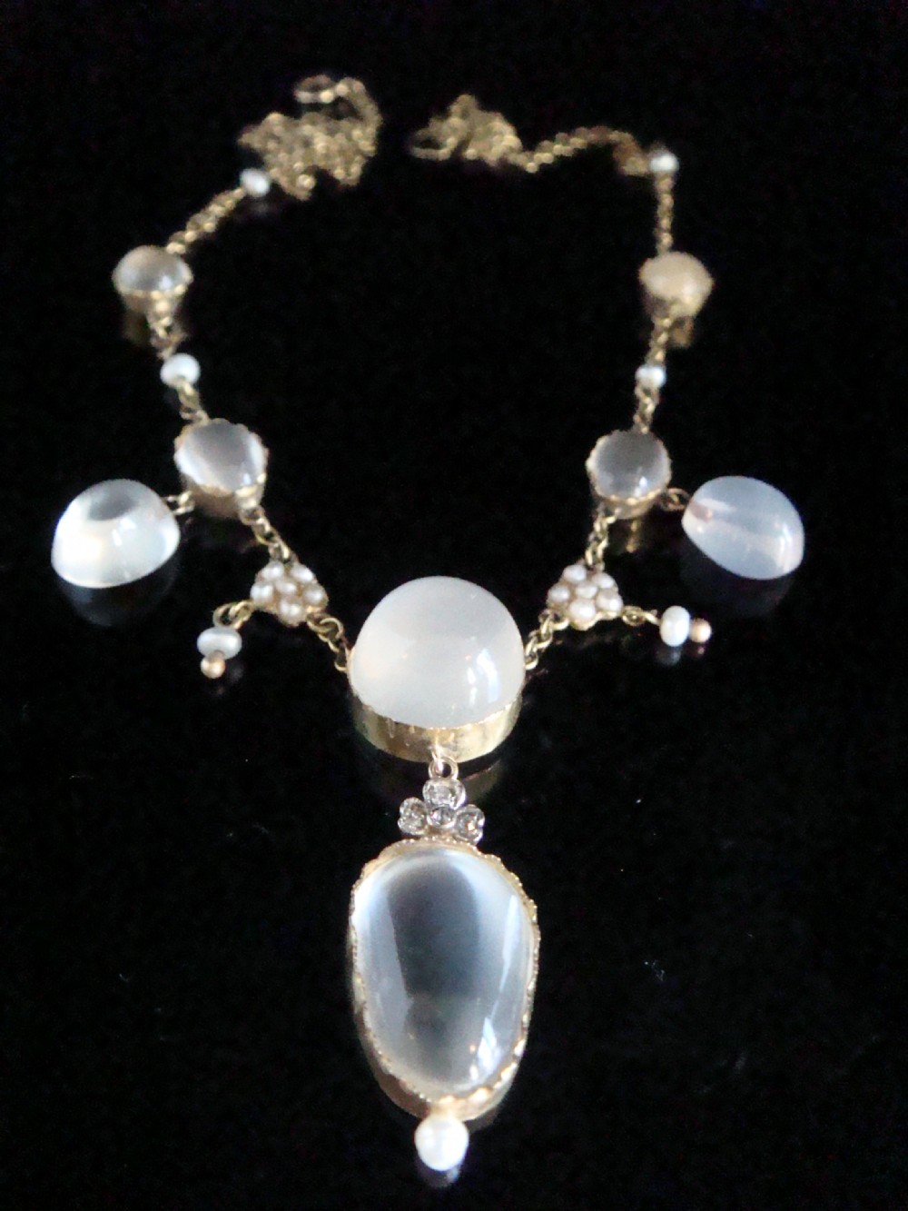 An Edwardian gold lavaliere necklace set with oval cabochon moonstones, seed pearl clusters, and a central drop pendant with diamond detail.