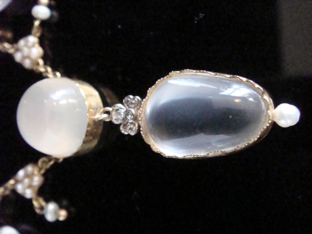 An Edwardian gold lavaliere necklace set with oval cabochon moonstones, seed pearl clusters, and a central drop pendant with diamond detail. View II