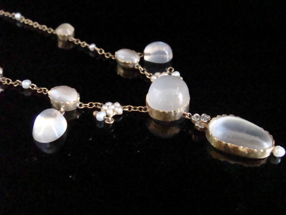 An Edwardian gold lavaliere necklace set with oval cabochon moonstones, seed pearl clusters, and a central drop pendant with diamond detail. View IV
