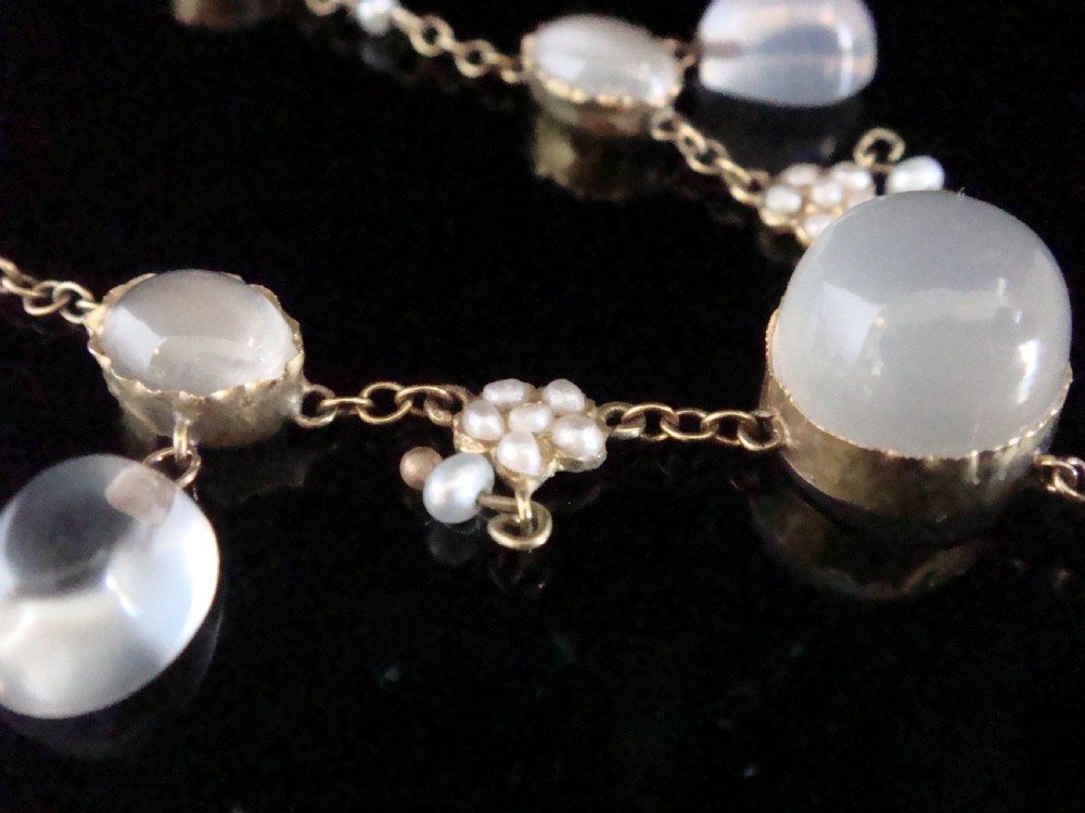 An Edwardian gold lavaliere necklace set with oval cabochon moonstones, seed pearl clusters, and a central drop pendant with diamond detail. View V