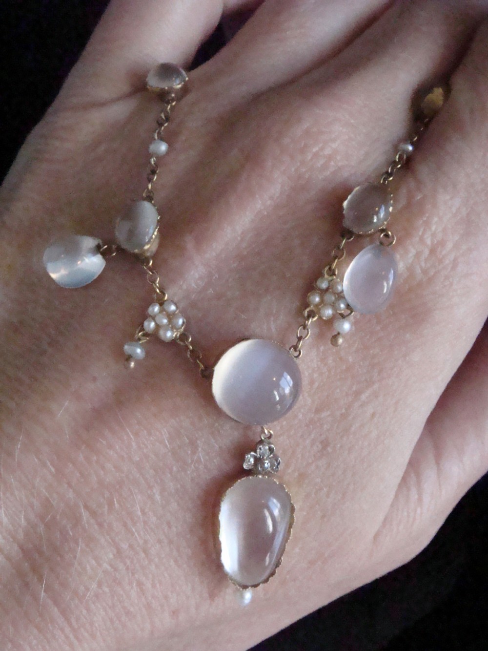 An Edwardian gold lavaliere necklace set with oval cabochon moonstones, seed pearl clusters, and a central drop pendant with diamond detail. View VII