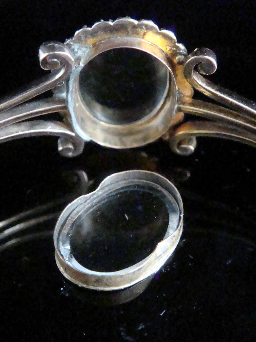 An antique 9ct yellow gold hinged bangle featuring a central oval glass shaker locket surrounded by a halo of small seed pearls. View V