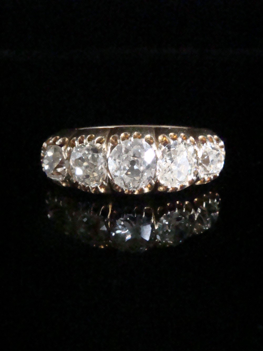 An early Victorian 18ct yellow gold ring featuring five graduated old-cut diamonds set horizontally along a carved gallery.