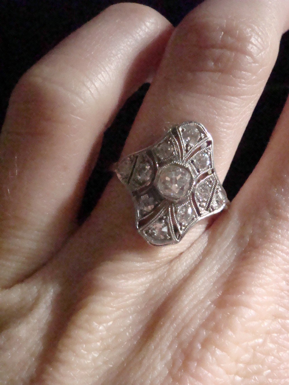An Edwardian platinum dress ring featuring a central old cut diamond surrounded by geometric diamond-paved sections with millegrain edging. View IV