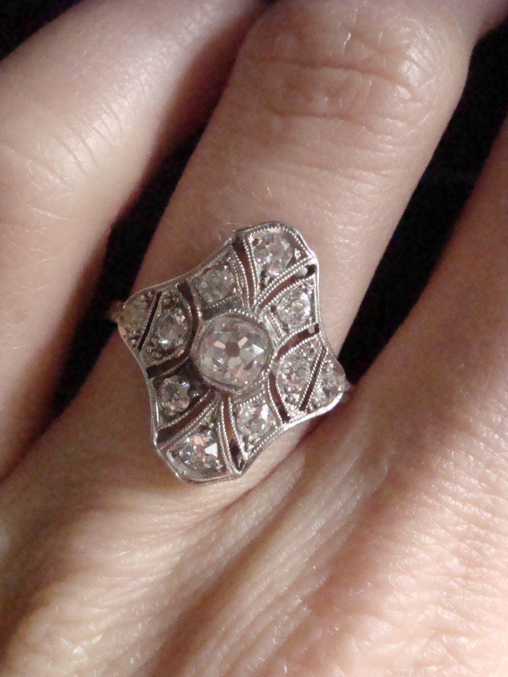 An Edwardian platinum dress ring featuring a central old cut diamond surrounded by geometric diamond-paved sections with millegrain edging. View V
