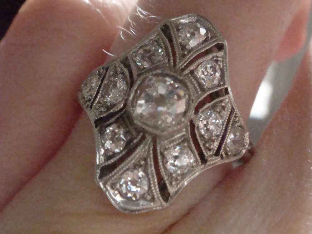 An Edwardian platinum dress ring featuring a central old cut diamond surrounded by geometric diamond-paved sections with millegrain edging. View VII