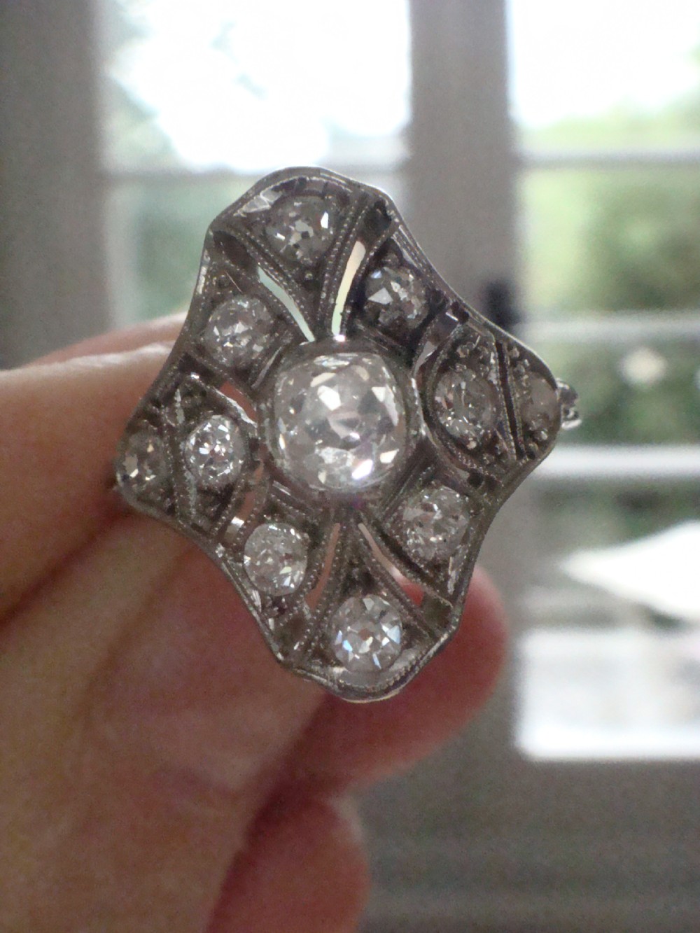 An Edwardian platinum dress ring featuring a central old cut diamond surrounded by geometric diamond-paved sections with millegrain edging. View VIII