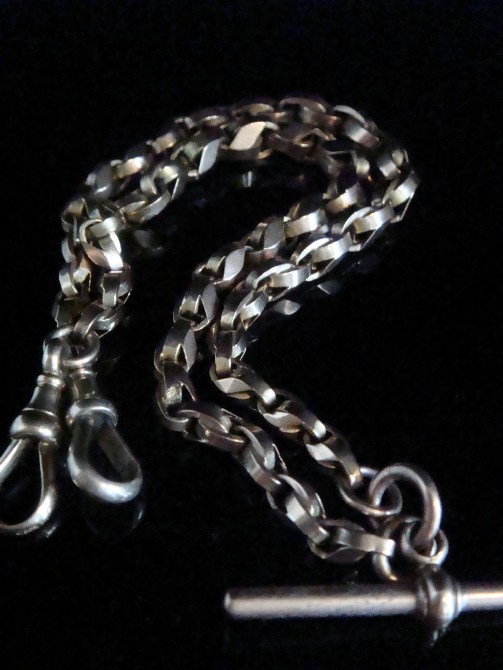 An Edwardian 9ct rose gold Albert chain featuring fancy interlocking links, dual dog clips, and a T-bar attachment.