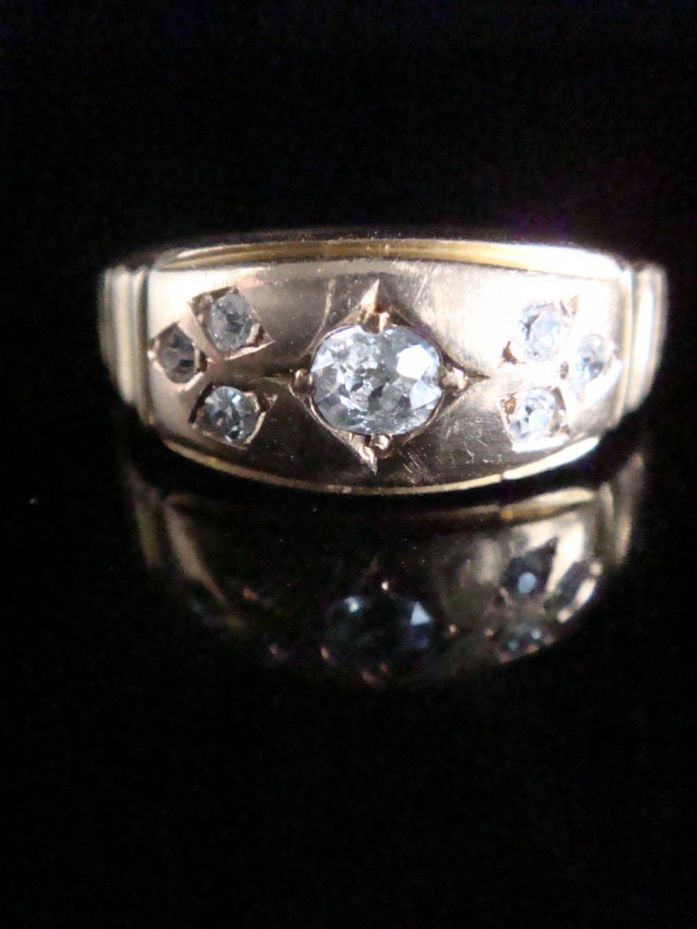 A Victorian 18ct yellow gold band featuring a central old cut diamond flanked by smaller flush-set diamonds in star-engraved settings.