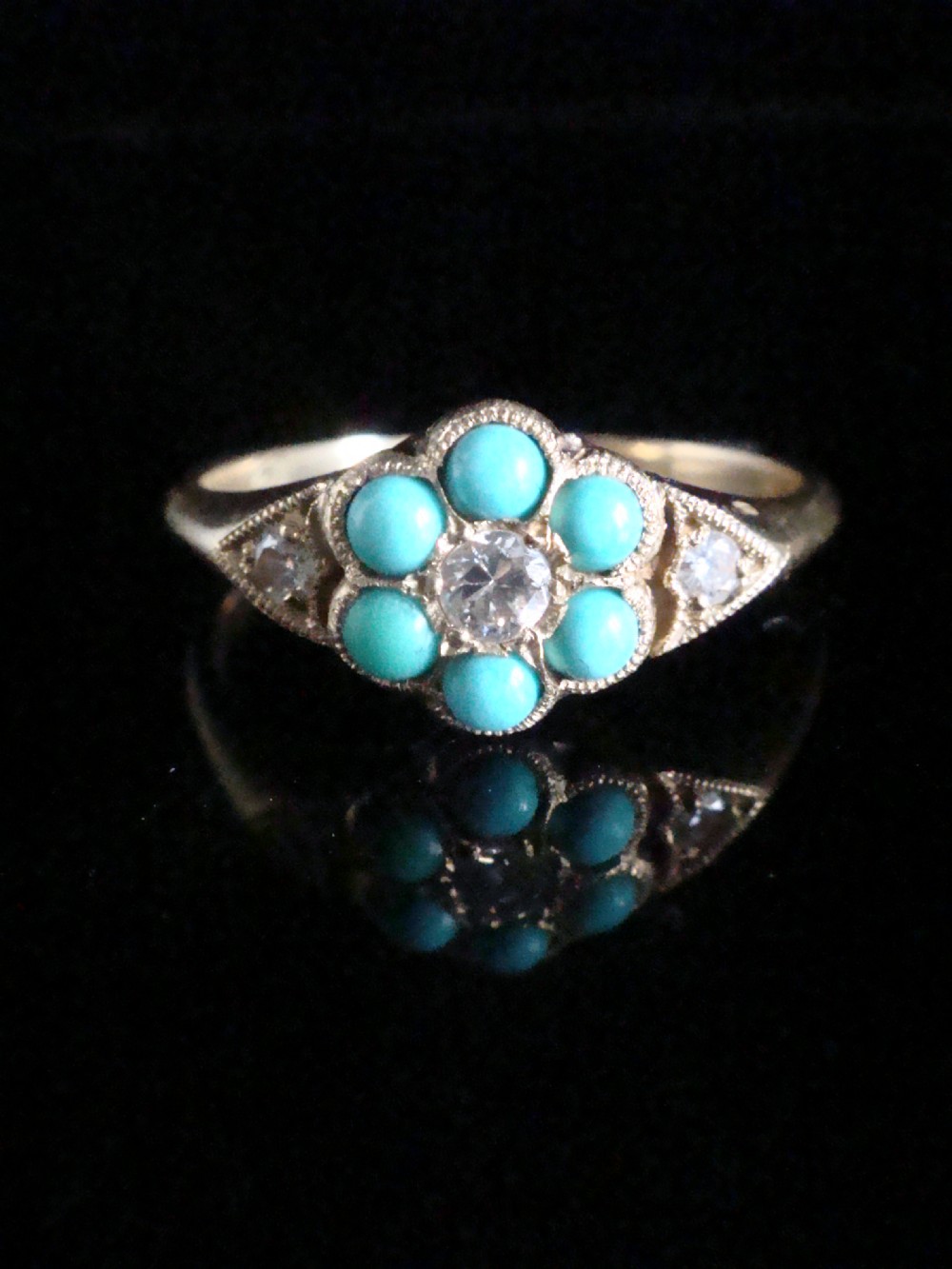 A Victorian 18ct yellow gold cluster ring featuring a central diamond surrounded by six turquoise cabochons with milgrain-detailed shoulders.