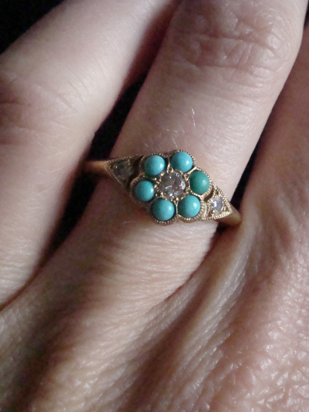 A Victorian 18ct yellow gold cluster ring featuring a central diamond surrounded by six turquoise cabochons with milgrain-detailed shoulders. View V
