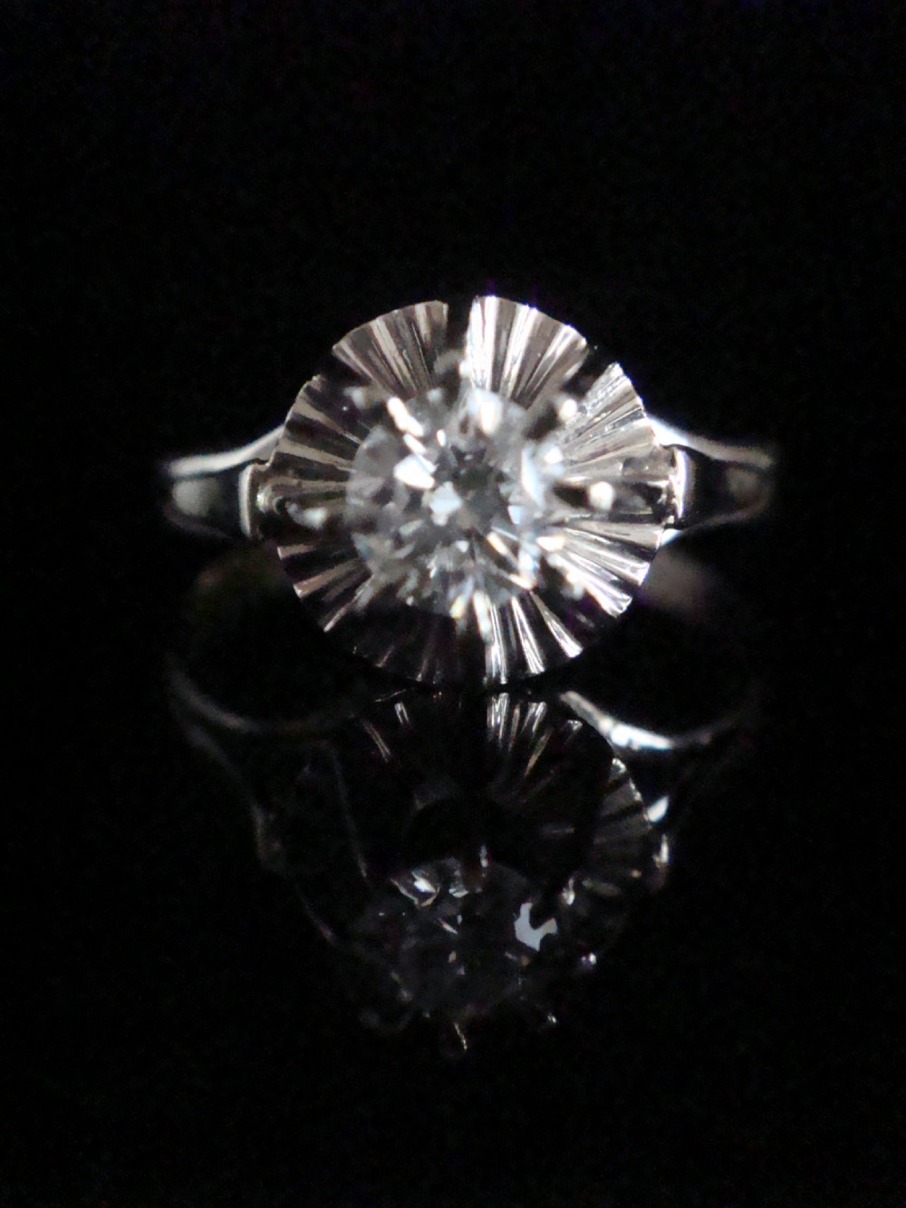 A vintage 18ct white gold solitaire ring featuring a central round diamond set within a fluted sunburst surround.