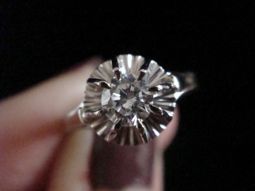 A vintage 18ct white gold solitaire ring featuring a central round diamond set within a fluted sunburst surround. View IV
