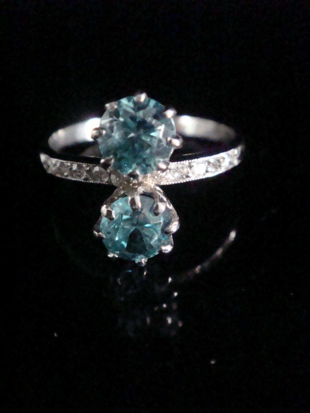 An Edwardian platinum ring featuring two round-cut blue zircon gemstones set vertically in a Toi et Moi design with diamond-set shoulders.