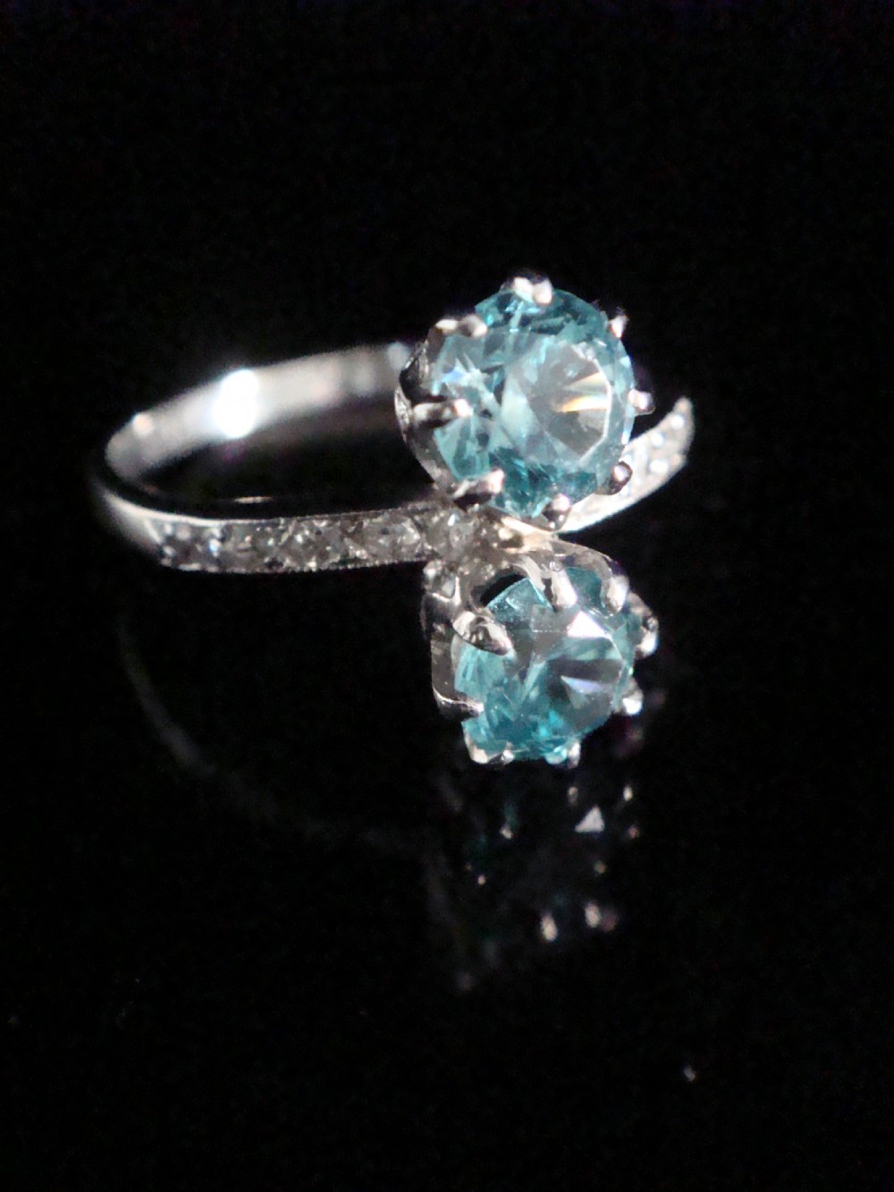 An Edwardian platinum ring featuring two round-cut blue zircon gemstones set vertically in a Toi et Moi design with diamond-set shoulders. View II