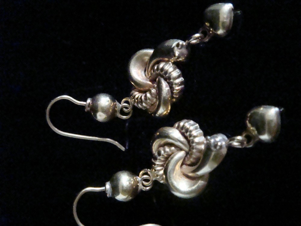 A pair of 9ct yellow gold drop earrings featuring an intertwined snake knot design suspended from shepherd hook fittings with dangling heart charms. View IV