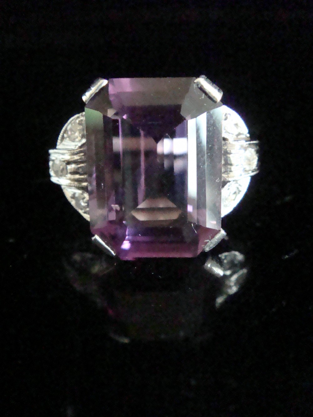 An Art Deco cocktail ring featuring a large emerald-cut purple amethyst flanked by diamond-set shoulders in an 18ct white gold setting.
