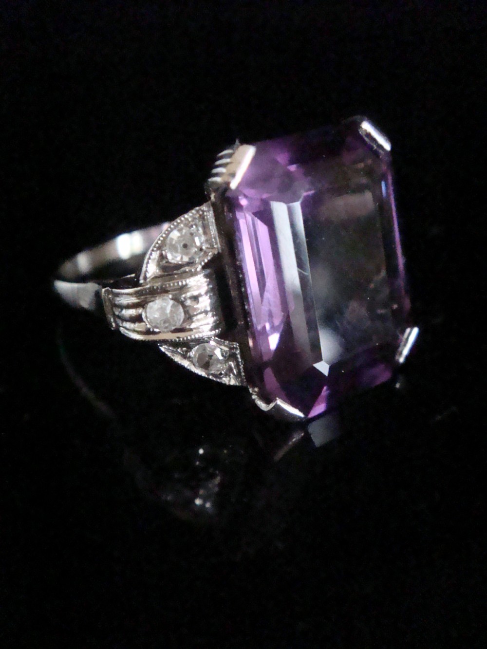 An Art Deco cocktail ring featuring a large emerald-cut purple amethyst flanked by diamond-set shoulders in an 18ct white gold setting. View II