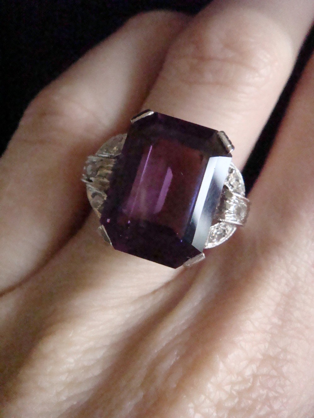 An Art Deco cocktail ring featuring a large emerald-cut purple amethyst flanked by diamond-set shoulders in an 18ct white gold setting. View V