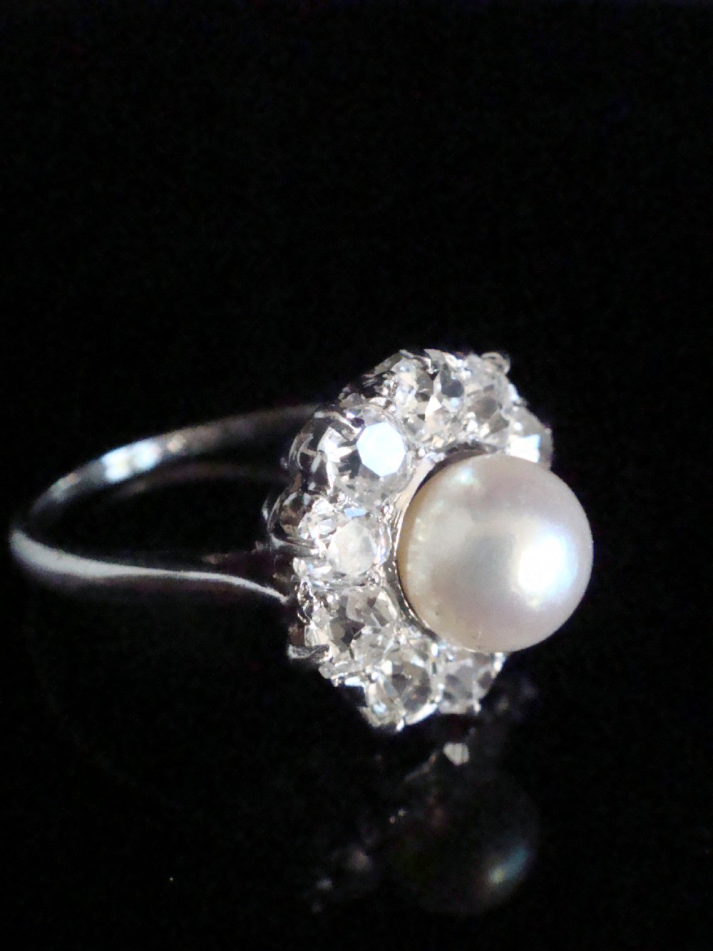 An Edwardian cluster ring featuring a central round pearl framed by a halo of old cut diamonds set in white metal. View III