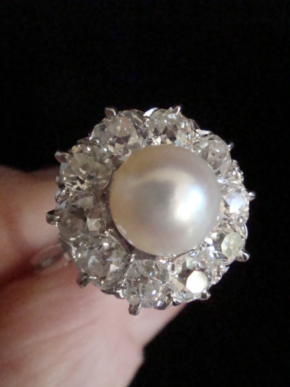 An Edwardian cluster ring featuring a central round pearl framed by a halo of old cut diamonds set in white metal. View IV