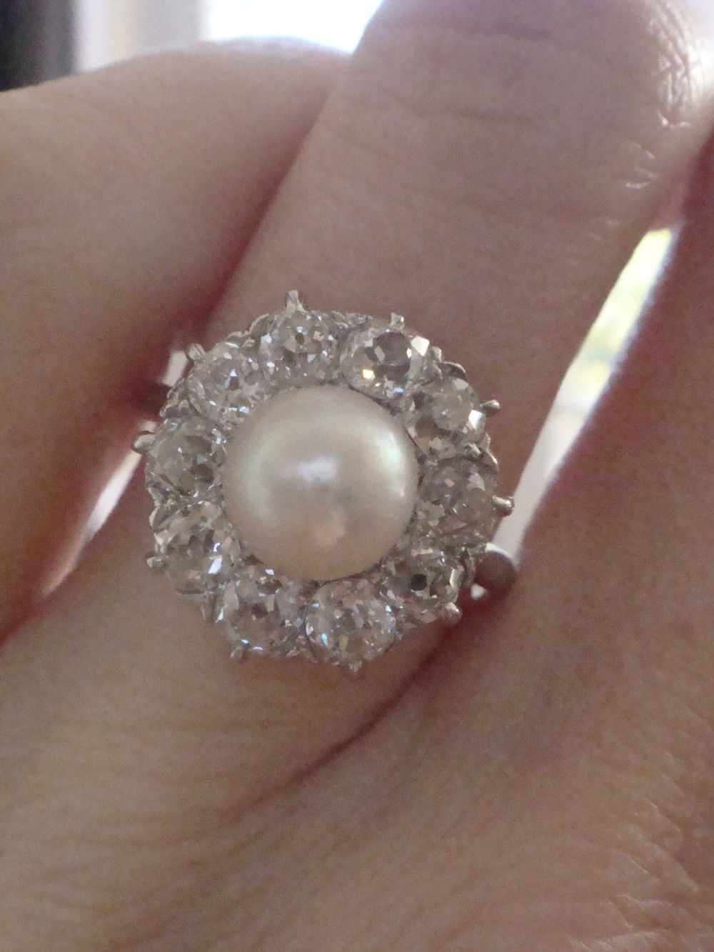 An Edwardian cluster ring featuring a central round pearl framed by a halo of old cut diamonds set in white metal. View VI