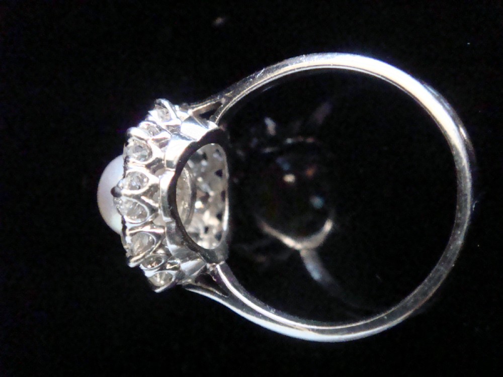 An Edwardian cluster ring featuring a central round pearl framed by a halo of old cut diamonds set in white metal. View VII
