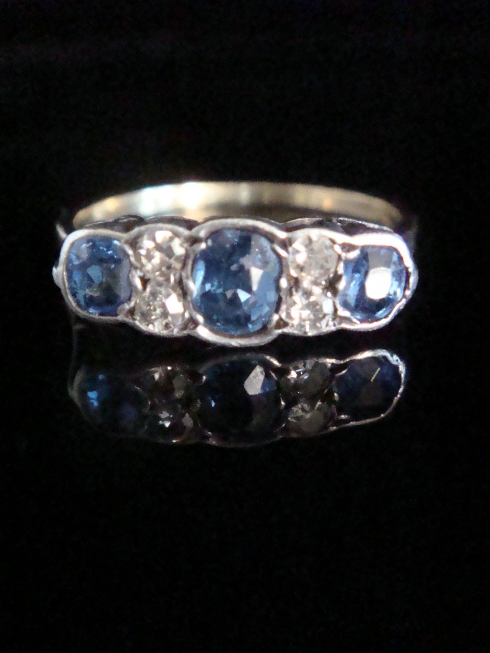 An Edwardian 18ct yellow gold five-stone ring featuring three oval blue sapphires alternating with two round diamonds set in a carved mount.