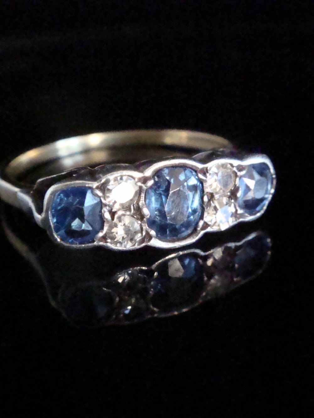 An Edwardian 18ct yellow gold five-stone ring featuring three oval blue sapphires alternating with two round diamonds set in a carved mount. View II