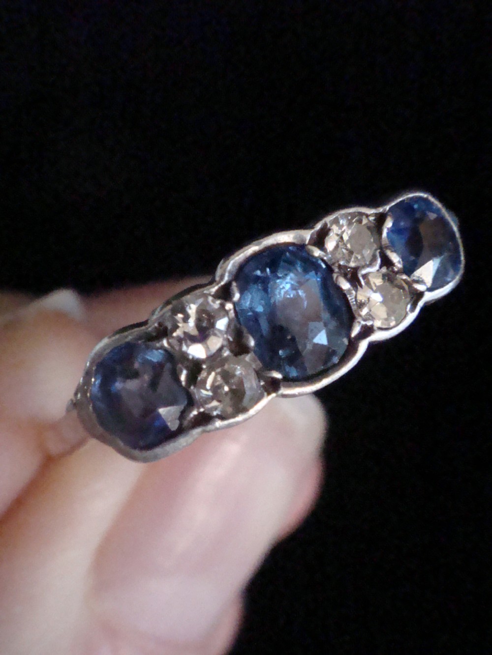 An Edwardian 18ct yellow gold five-stone ring featuring three oval blue sapphires alternating with two round diamonds set in a carved mount. View IV