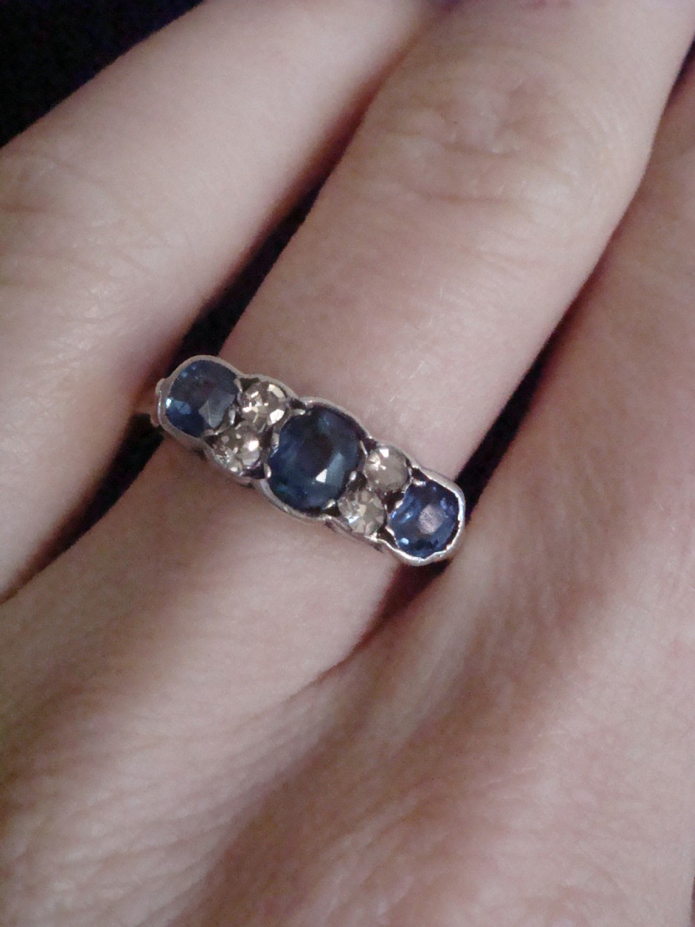An Edwardian 18ct yellow gold five-stone ring featuring three oval blue sapphires alternating with two round diamonds set in a carved mount. View V
