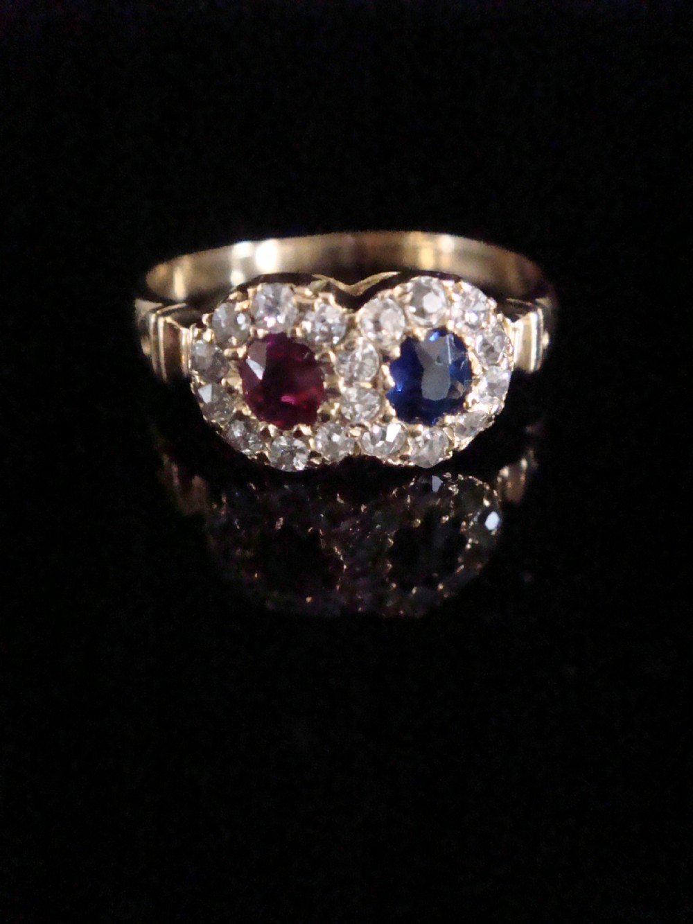 An Edwardian 18ct yellow gold Toi et Moi ring featuring a central ruby and sapphire, each encircled by a halo of old cut diamonds.