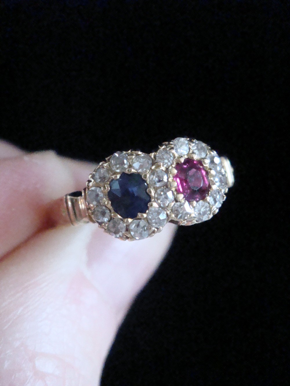 An Edwardian 18ct yellow gold Toi et Moi ring featuring a central ruby and sapphire, each encircled by a halo of old cut diamonds. View IV
