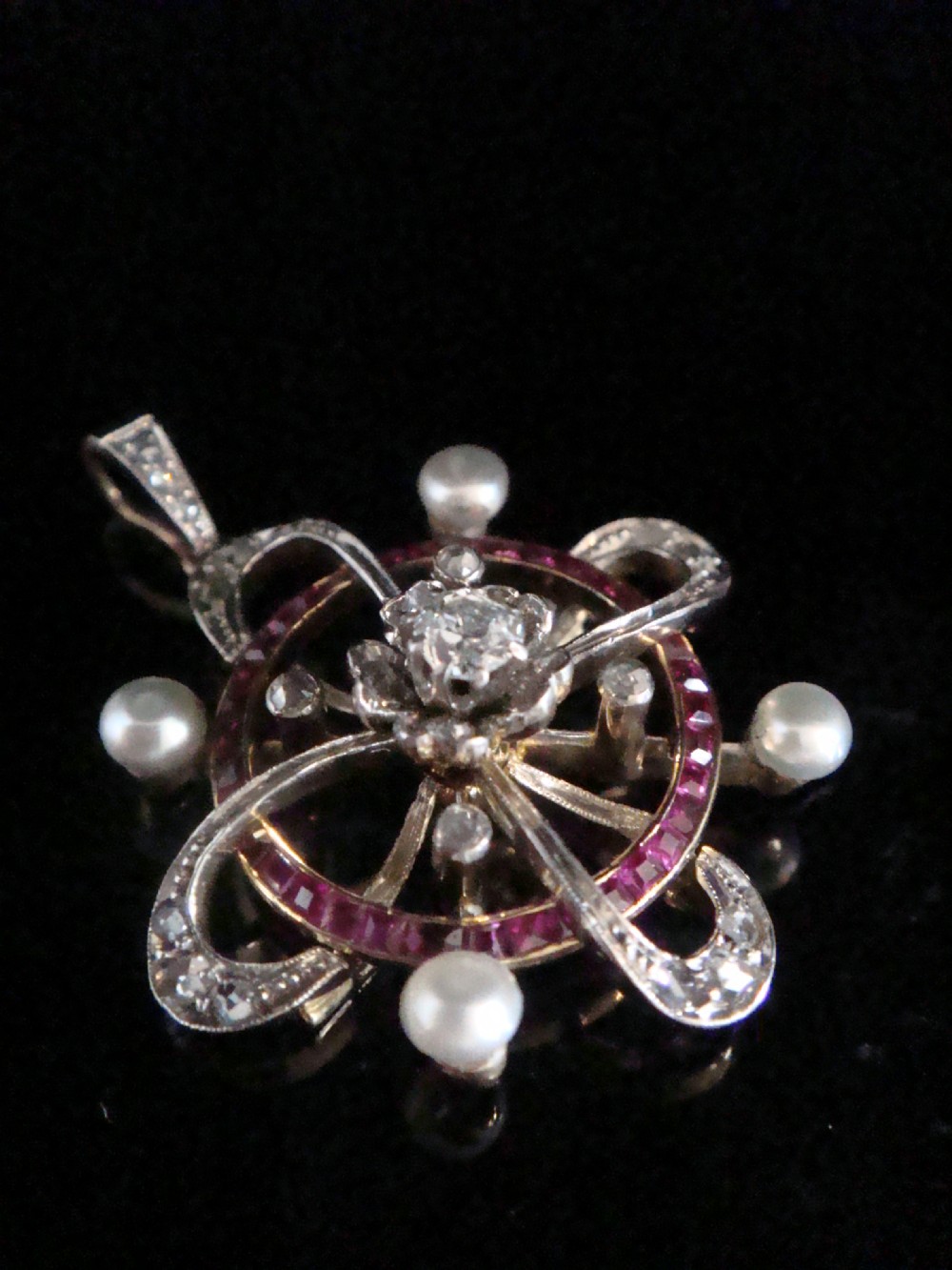 An 18ct gold Victorian openwork pendant set with a central diamond, four natural pearls, calibre-cut rubies, and rose-cut diamonds.