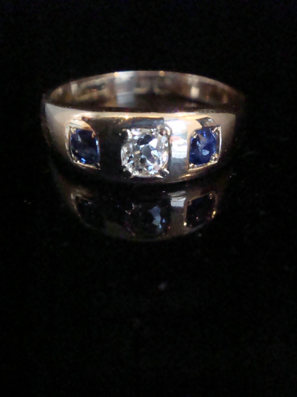 An antique 18ct yellow gold gypsy ring set with a central old cut diamond flanked by two round blue sapphires flush within the band.