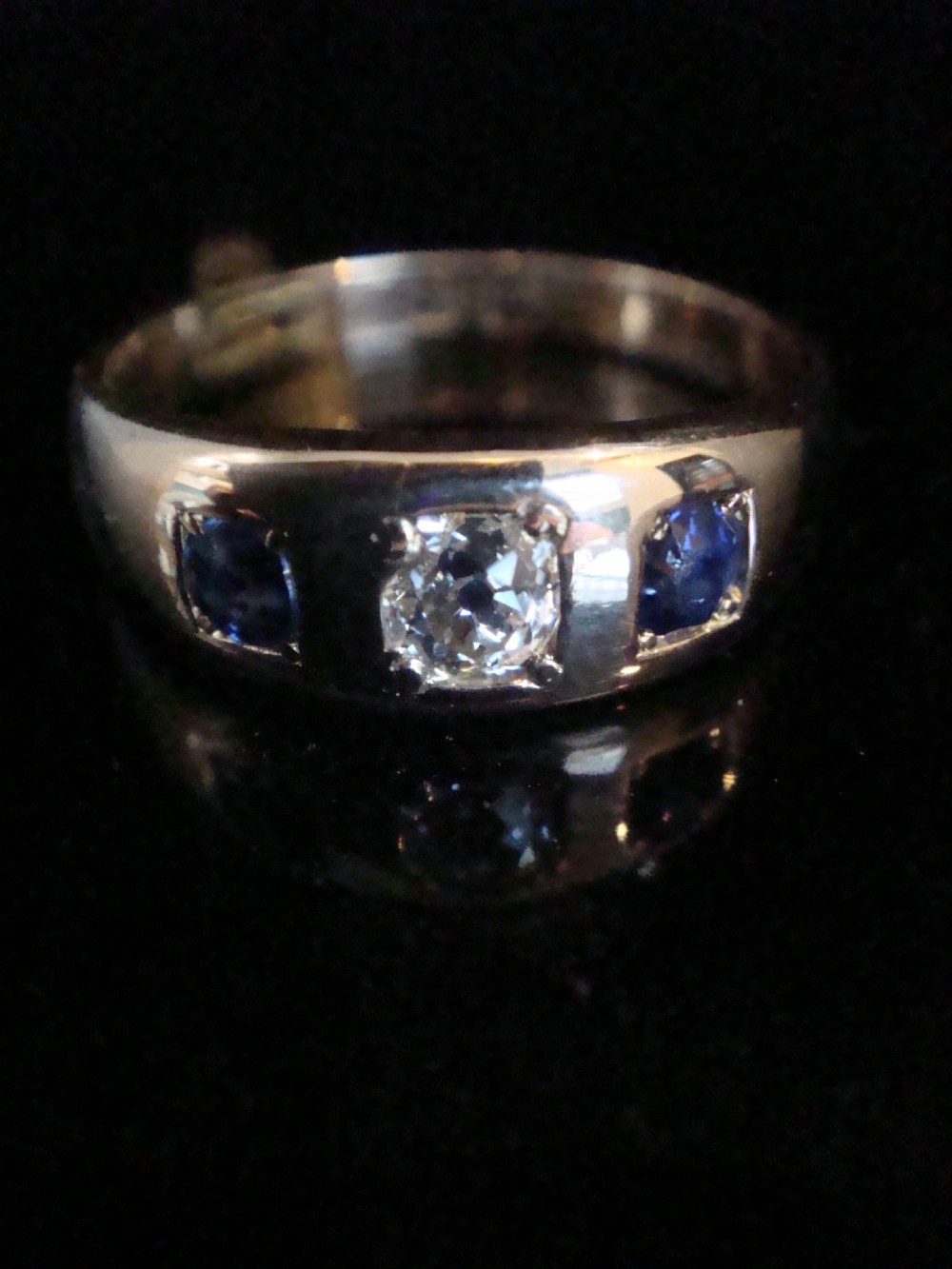 An antique 18ct yellow gold gypsy ring set with a central old cut diamond flanked by two round blue sapphires flush within the band. View II