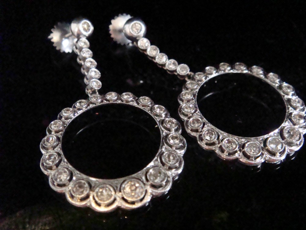 Pair of Edwardian style platinum and 18ct white gold drop earrings featuring circular halo pendants set with old cut diamonds suspended from articulated linear stems.