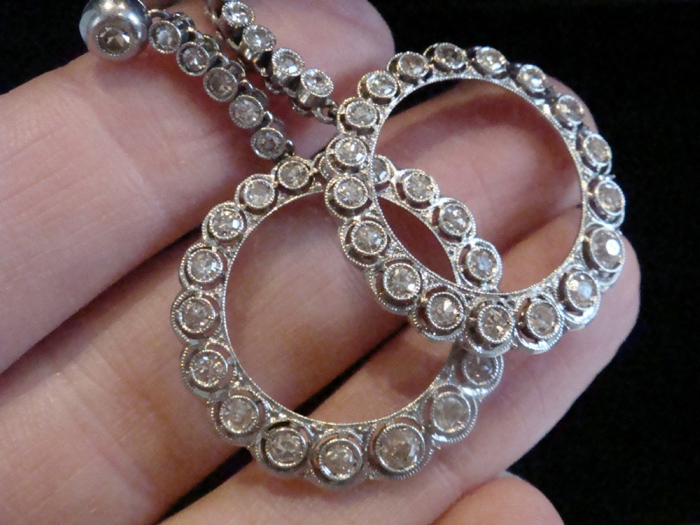 Pair of Edwardian style platinum and 18ct white gold drop earrings featuring circular halo pendants set with old cut diamonds suspended from articulated linear stems. View II