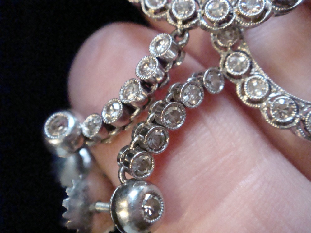 Pair of Edwardian style platinum and 18ct white gold drop earrings featuring circular halo pendants set with old cut diamonds suspended from articulated linear stems. View IV