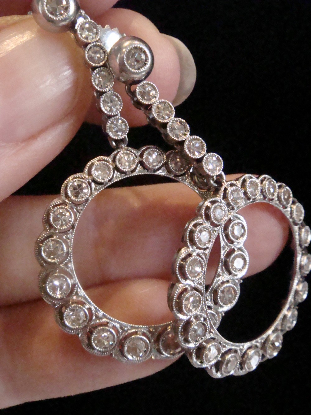 Pair of Edwardian style platinum and 18ct white gold drop earrings featuring circular halo pendants set with old cut diamonds suspended from articulated linear stems. View VI