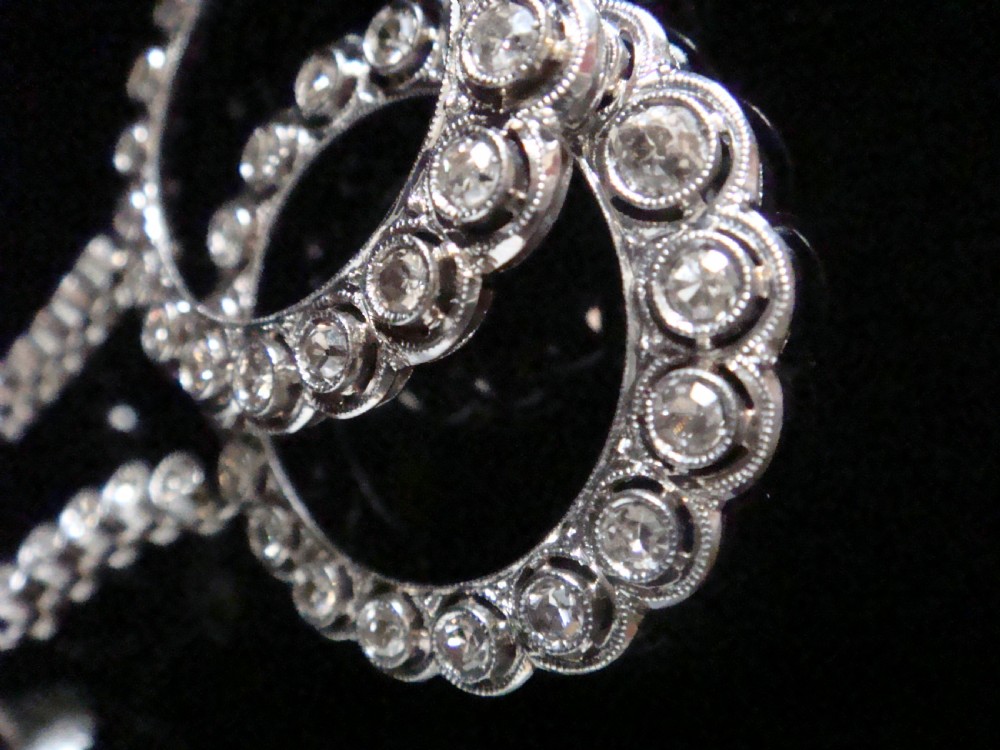 Pair of Edwardian style platinum and 18ct white gold drop earrings featuring circular halo pendants set with old cut diamonds suspended from articulated linear stems. View VII