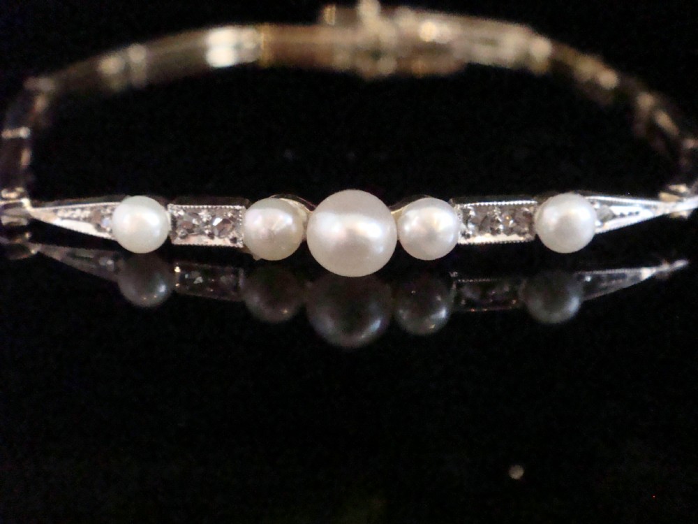 An Edwardian 18ct yellow gold line bracelet featuring a central row of five graduated saltwater pearls interspersed with diamond-set rectangular links.