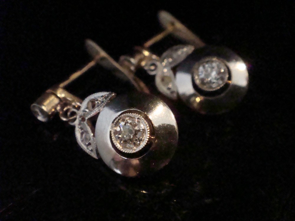 A pair of French Edwardian 18ct yellow gold and platinum drop earrings featuring central old-cut diamonds set within circular dished mounts with millegrain edges.
