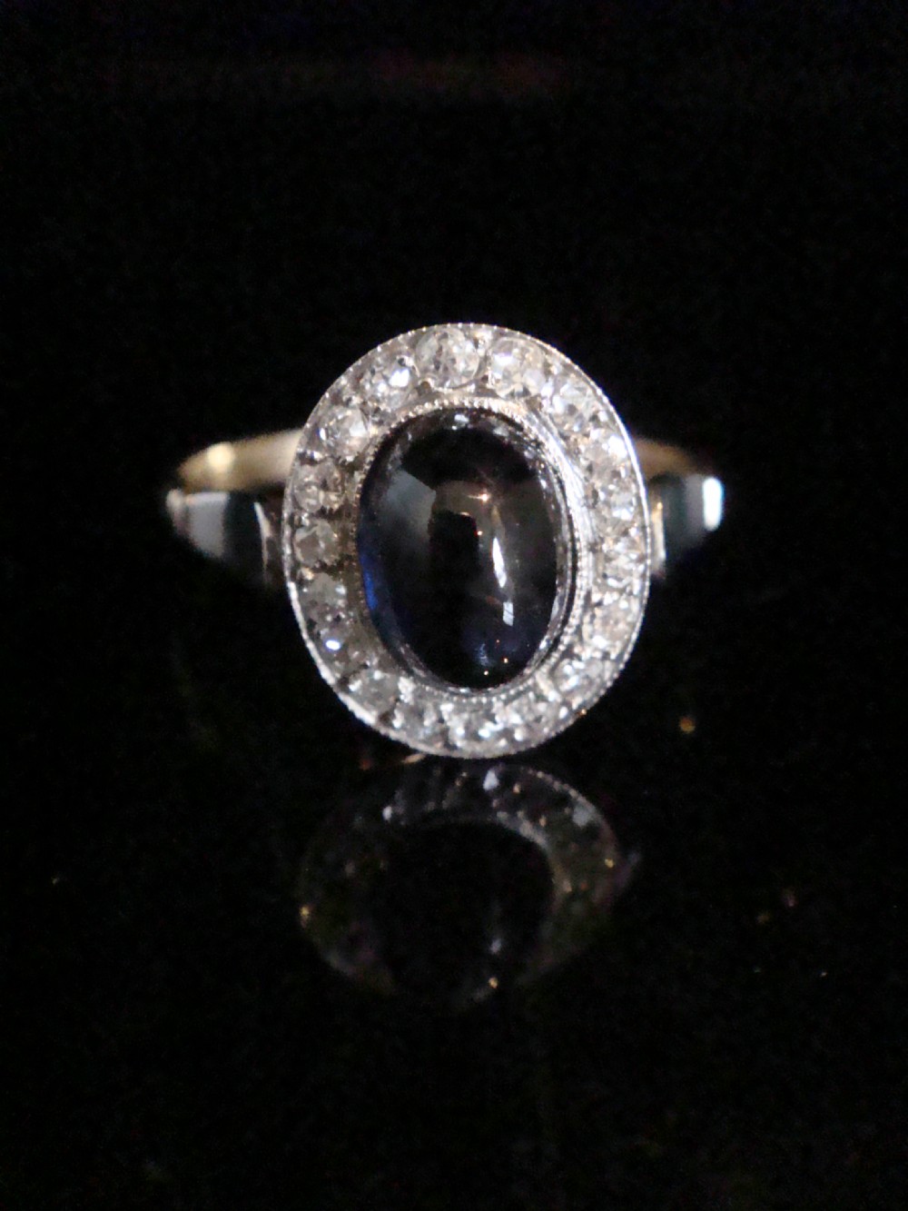 An Edwardian platinum and 18ct yellow gold cluster ring featuring a central oval cabochon sapphire surrounded by a halo of rose cut diamonds. View II