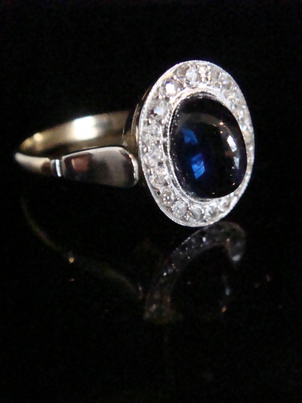 An Edwardian platinum and 18ct yellow gold cluster ring featuring a central oval cabochon sapphire surrounded by a halo of rose cut diamonds.