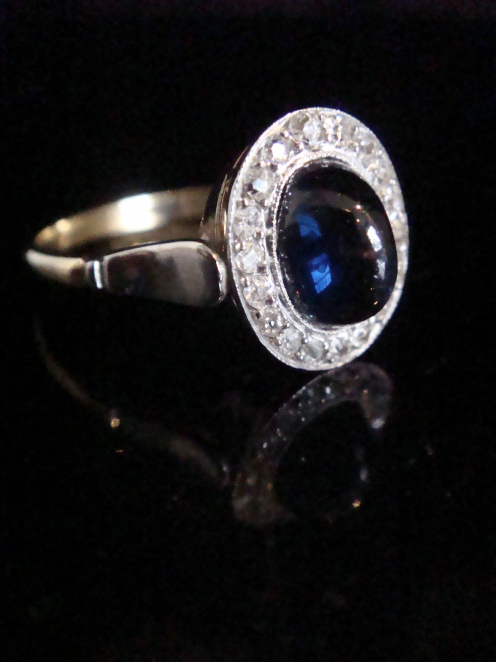 An Edwardian platinum and 18ct yellow gold cluster ring featuring a central oval cabochon sapphire surrounded by a halo of rose cut diamonds. View III