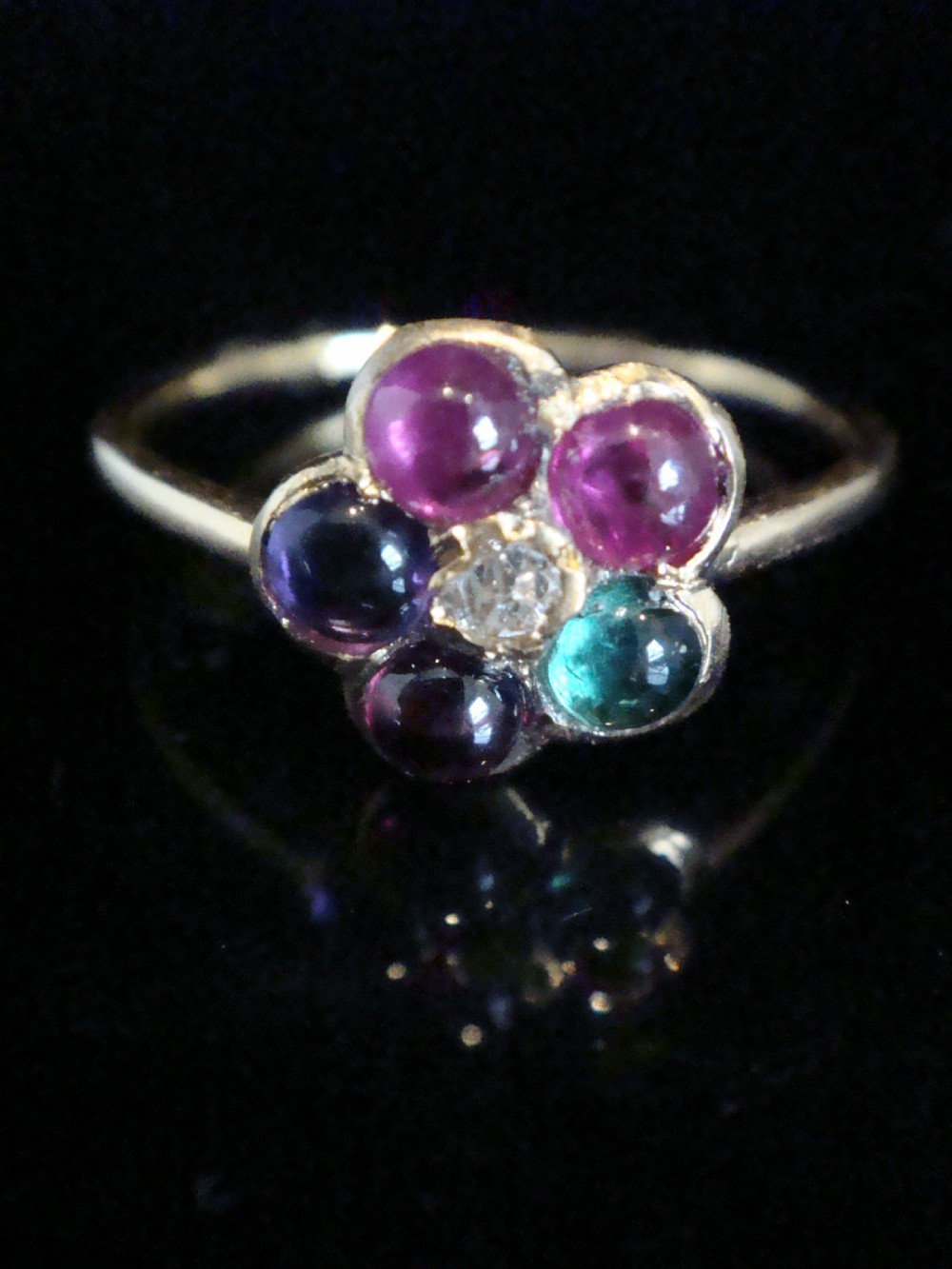 A Victorian 15ct gold flower cluster ring set with cabochon gemstones surrounding a central diamond.