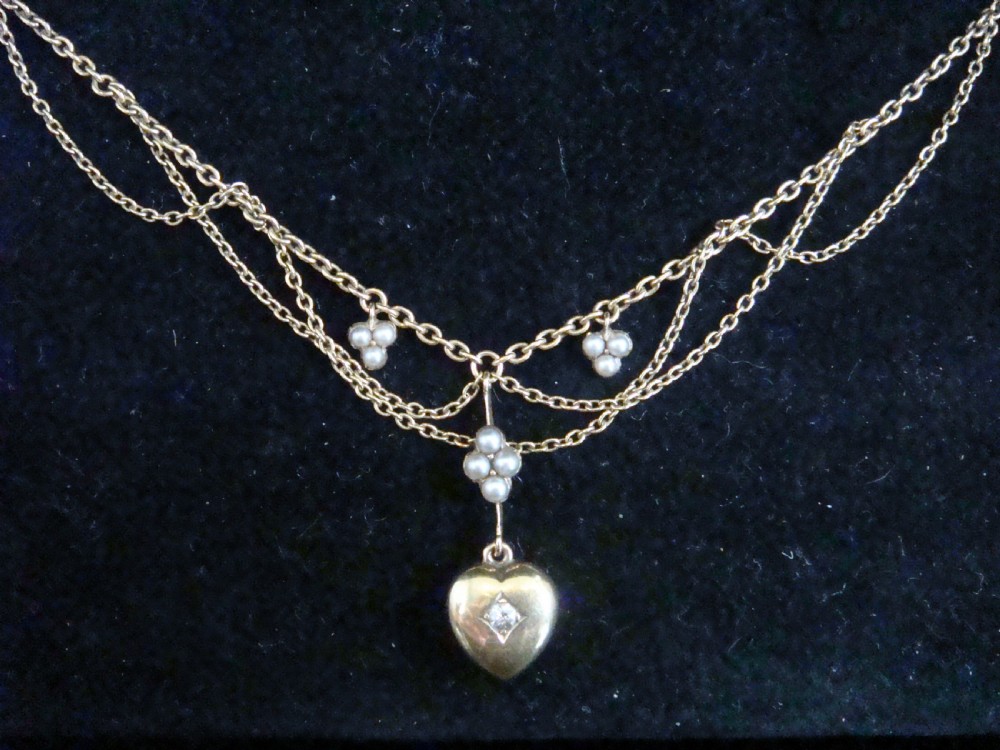 A Victorian yellow gold lavaliere necklace featuring draped swag chains, seed pearl clusters, and a central heart pendant inset with a diamond.