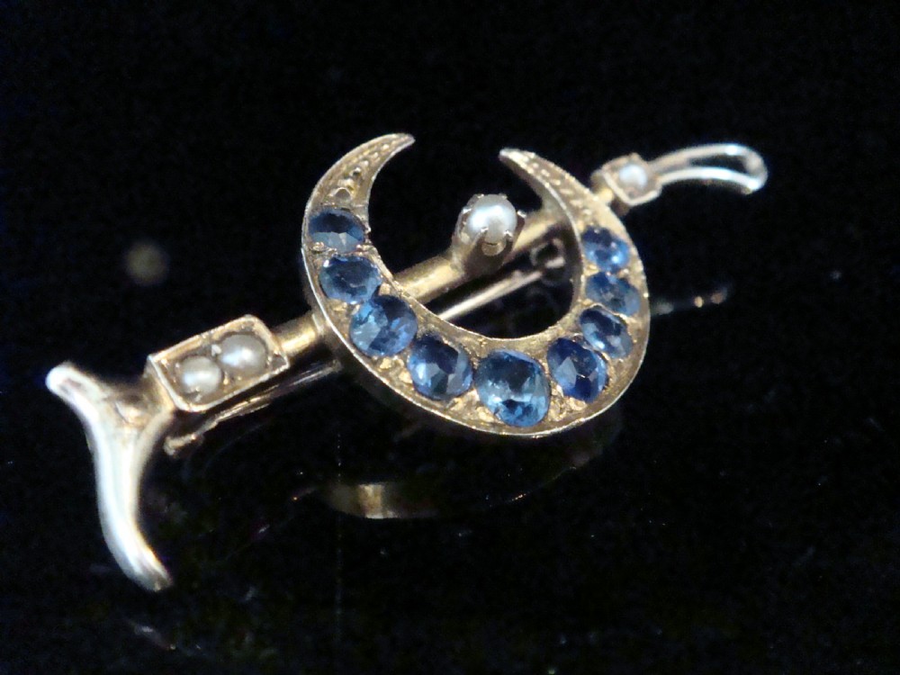 An Edwardian 9ct yellow gold bar brooch featuring a crescent moon motif set with blue sapphires and accented with seed pearls. View II